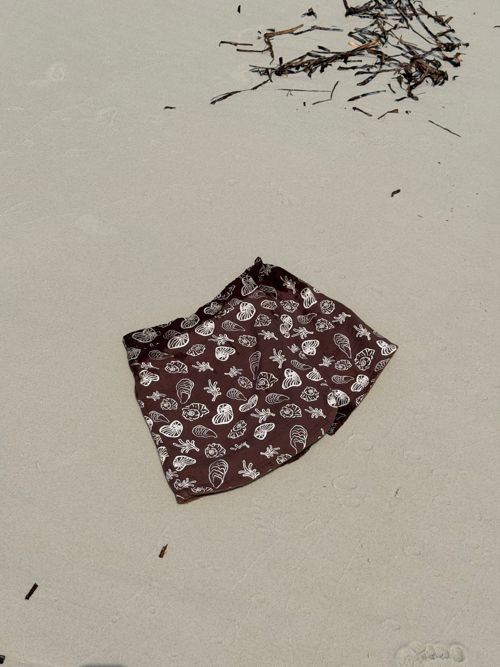 Brown fabric with white shell patterns in the shape of a Skort for women to wear over their swimwear that is made from Terry towelling on a sandy surface
