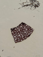Brown fabric with white shell patterns in the shape of a Skort for women to wear over their swimwear that is made from Terry towelling on a sandy surface